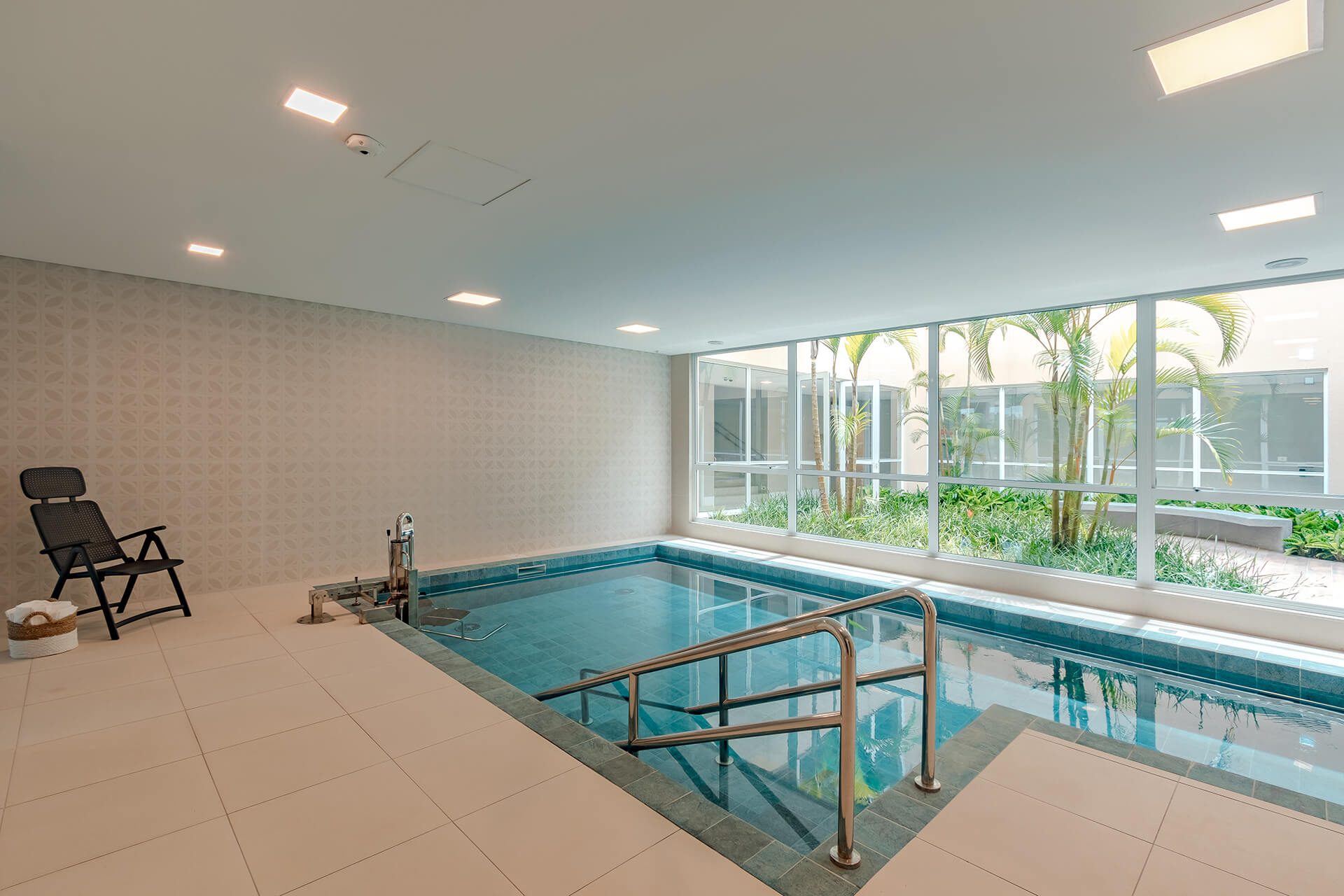 Piscina coberta com corrimão de apoio e vista para o jardim
