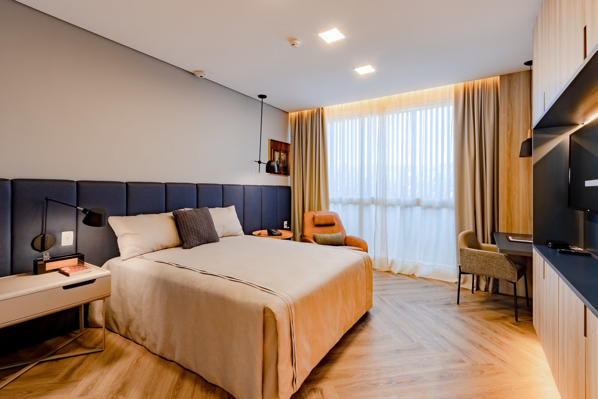Suíte com cama de casal, poltrona e cortinas claras
